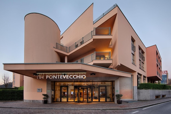 A modern hotel with a curved facade, multiple balconies, and a prominent entrance with glass doors. - NH Lecco Pontevecchio (Lecco)