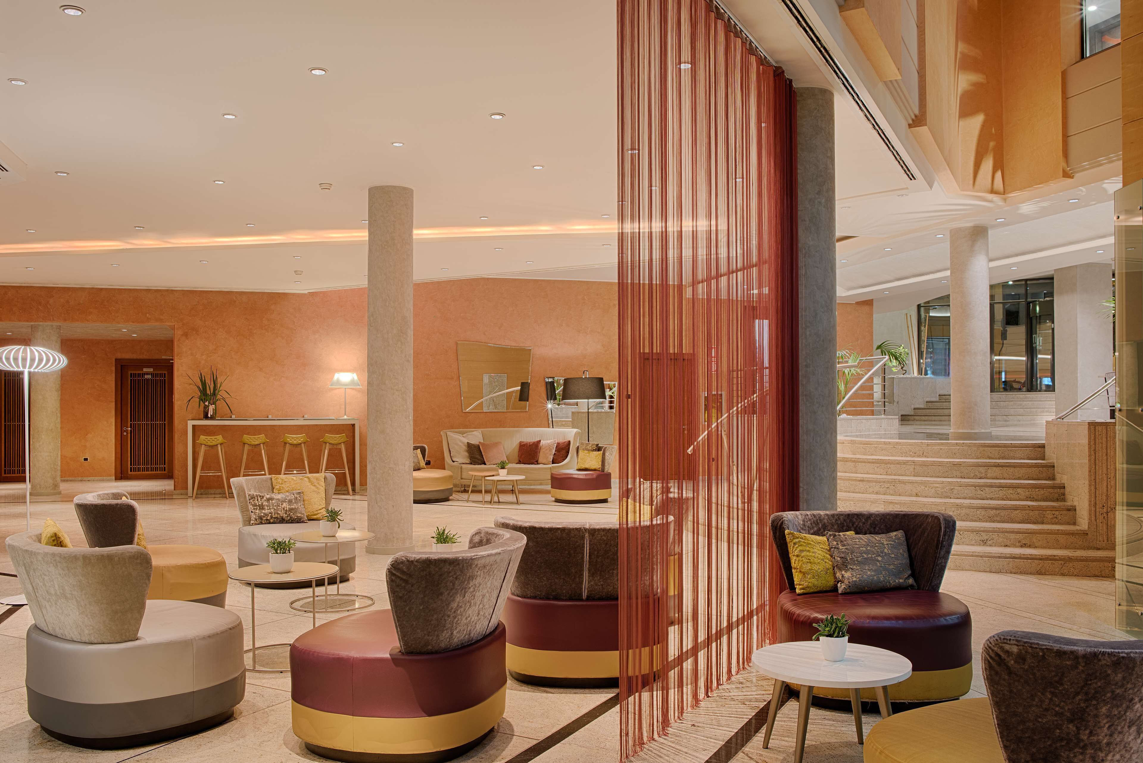 A modern lobby with seating areas, a reception desk, and a staircase.