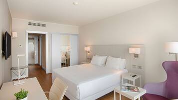 Habitación de hotel con cama, mesitas de noche, escritorio, silla, televisor y lámpara.