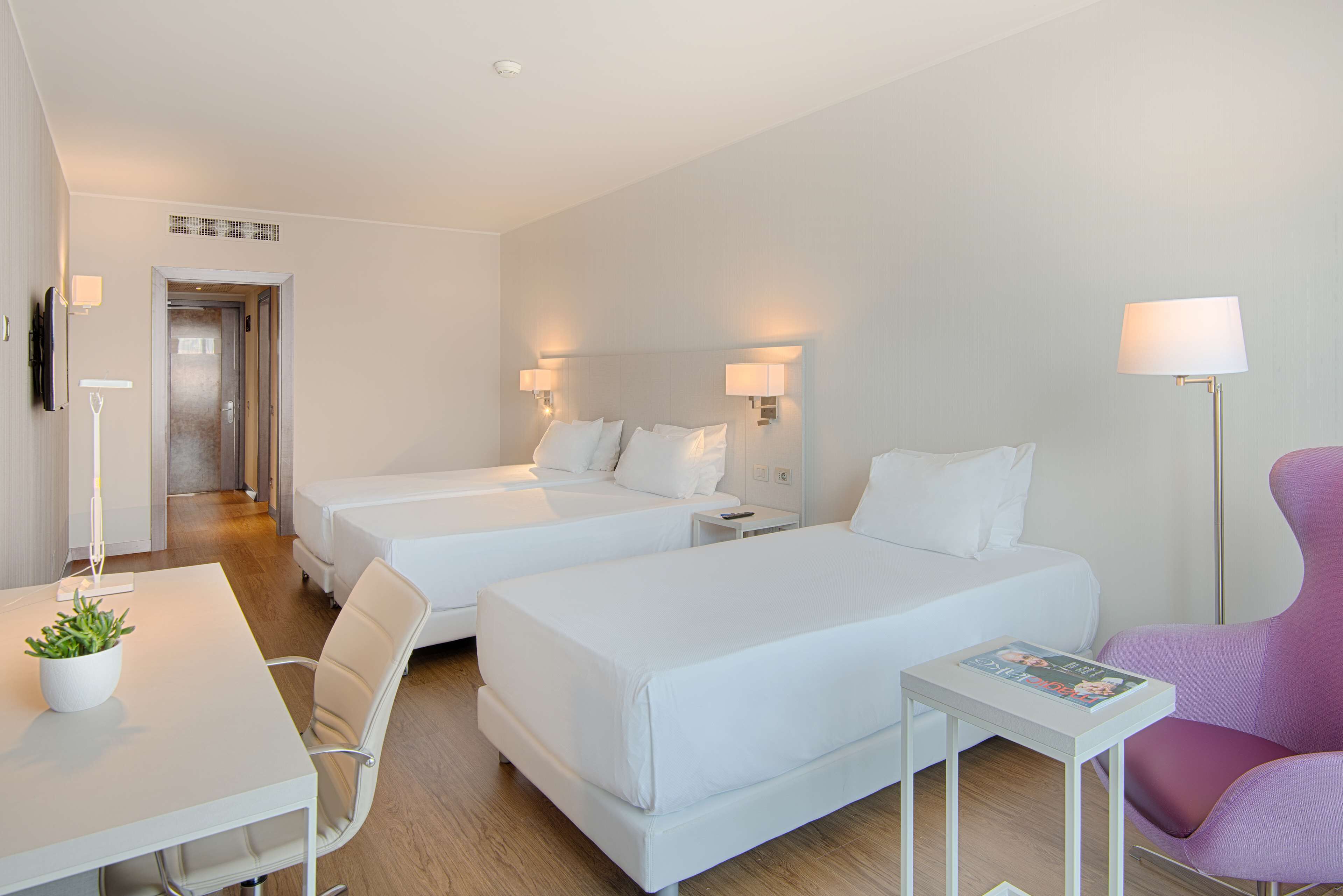 Et hotelværelse med to senge, et skrivebord, en stol, et lille bord og en lampe.