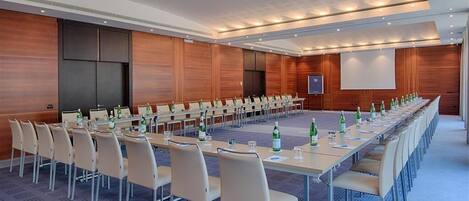 A conference room with long tables, chairs, and a projector screen.