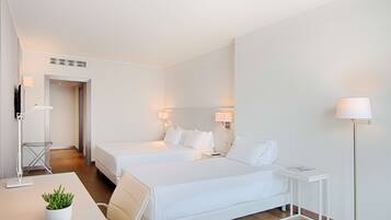 A hotel room with two beds, a desk, a plant, and a floor lamp.