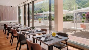 Un restaurant avec une longue table dressée pour le dîner et de grandes fenêtres donnant sur un paysage montagneux.