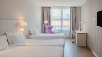 Ein Hotelzimmer mit zwei Betten, einem Schreibtisch, einem Sessel, einem Fernseher und einem Fenster mit Vorhängen.