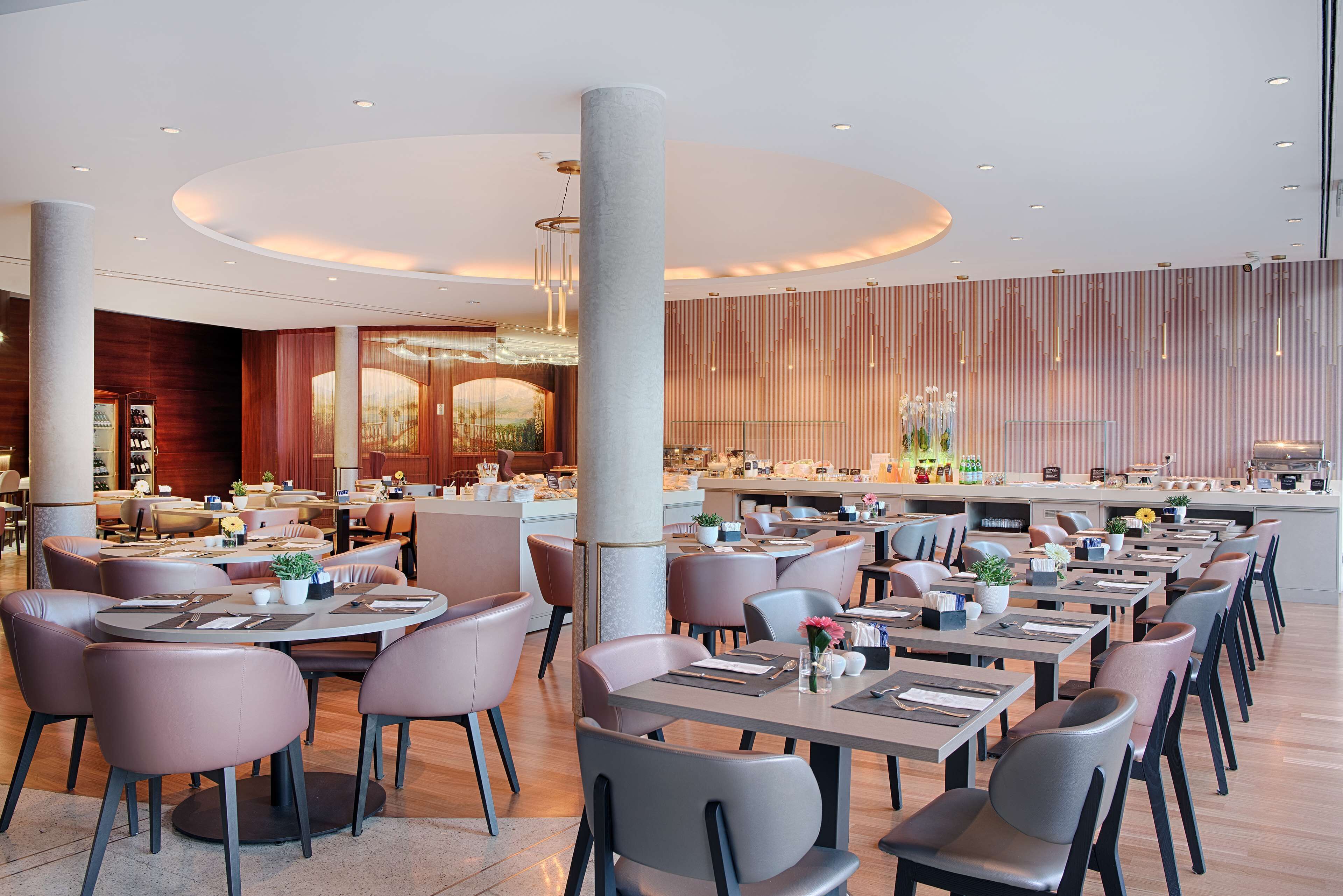 A modern restaurant with round tables and chairs, a central bar area, and a decorative ceiling.