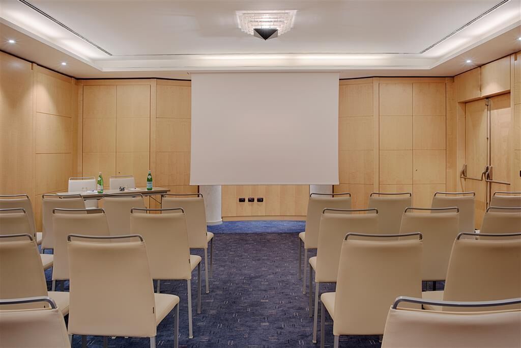 A conference room with rows of chairs, a projector screen, and a podium.