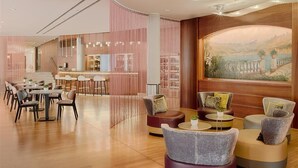 Un hall d’hôtel moderne doté d’un bar, d’espaces aménagés pour s’asseoir et d’une grande fresque murale représentant un paysage.