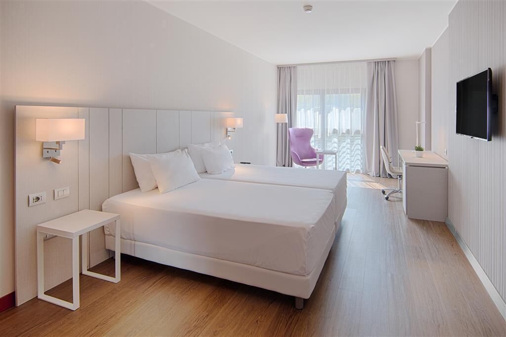 A modern hotel room with a large bed, bedside tables, a desk, and a TV.