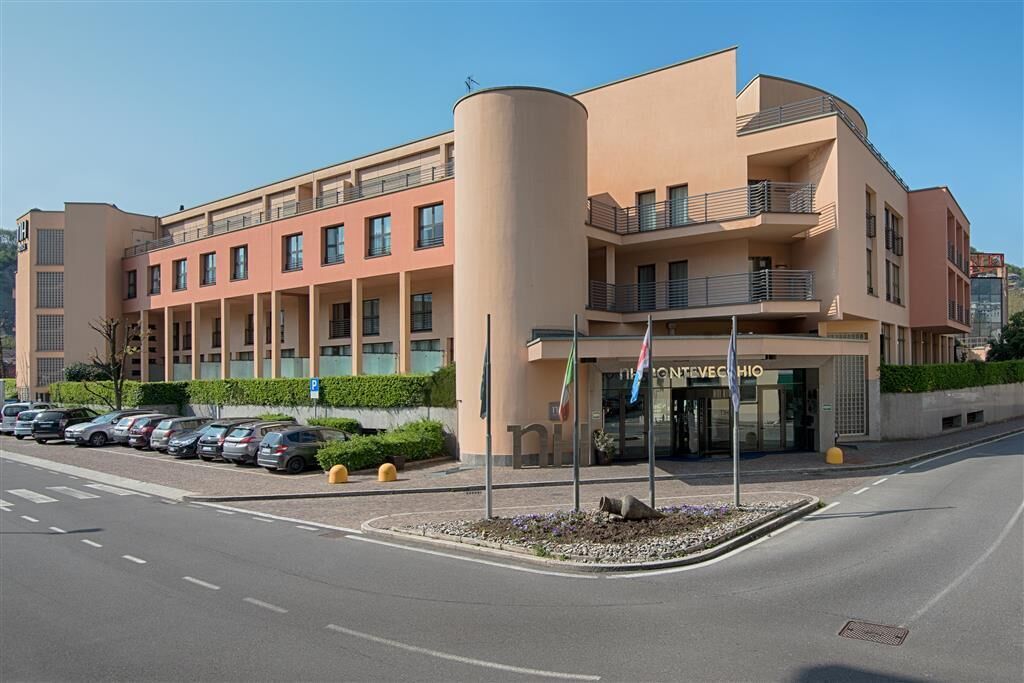 Un hôtel moderne à la façade incurvée, doté de nombreux balcons et d’un parking où sont stationnées plusieurs voitures.