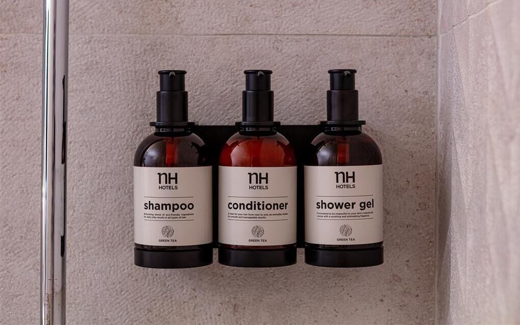 Three bottles of hotel amenities: shampoo, conditioner, and shower gel, labeled with 'nh hotels' and 'green tea'.
