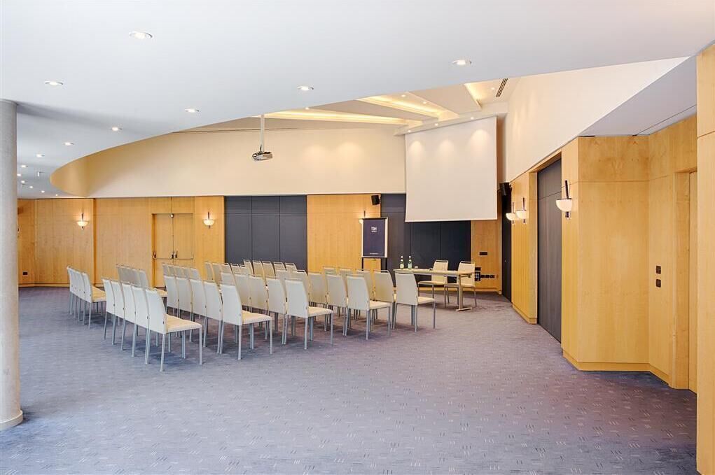 A conference room with rows of chairs, a projector screen, and a table with water bottles.