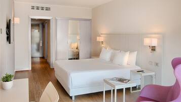A modern hotel room with a large bed, bedside tables, a desk, a chair, and a pink chair.
