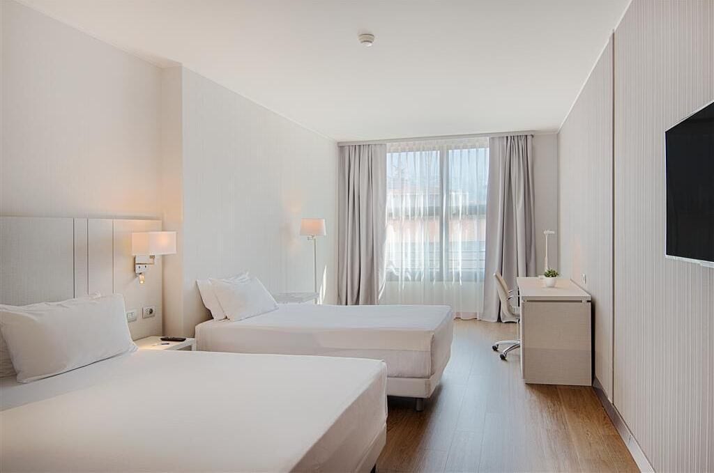 Una habitación de hotel con dos camas, un escritorio, una silla y un televisor.