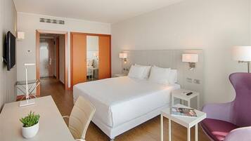 A hotel room with a large bed, a desk with a plant, a chair, a TV, and a lamp.
