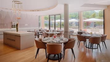 Un comedor moderno con mesas y sillas redondas, ventanas amplias y una isla central con un jarrón de flores.