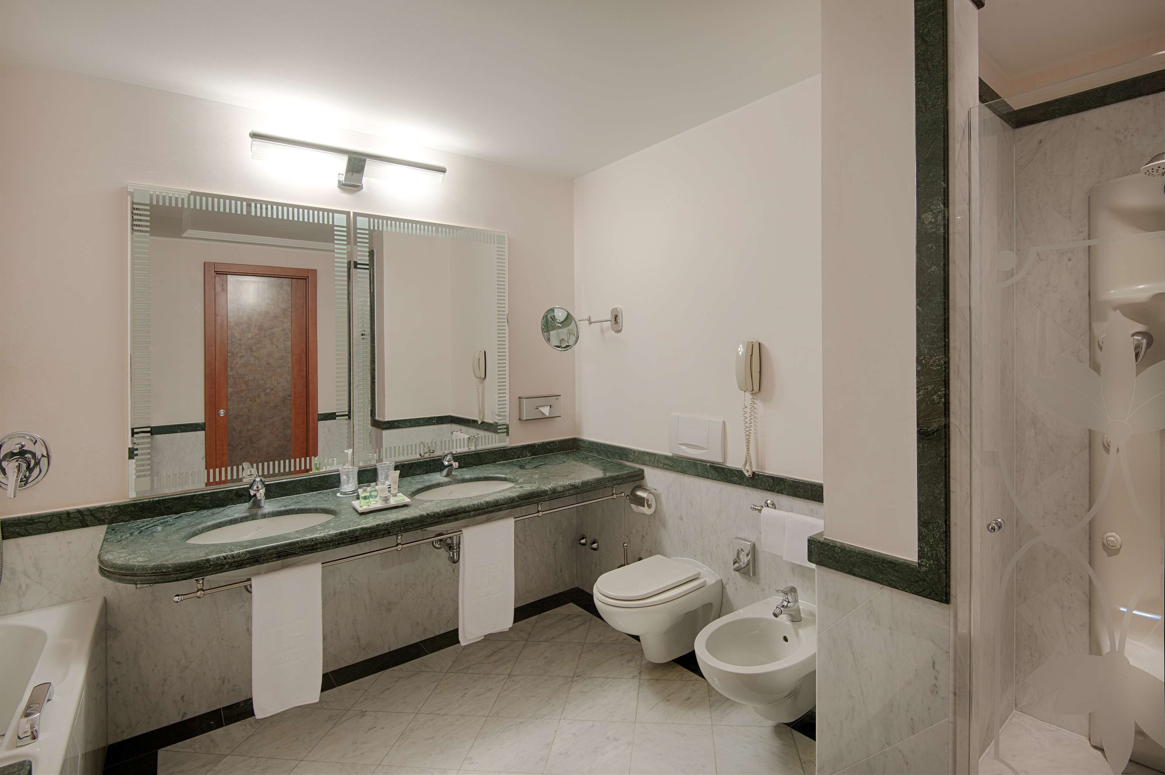 Um banheiro moderno com uma bancada com duas pias, vaso sanitário, bidê e área de chuveiro.