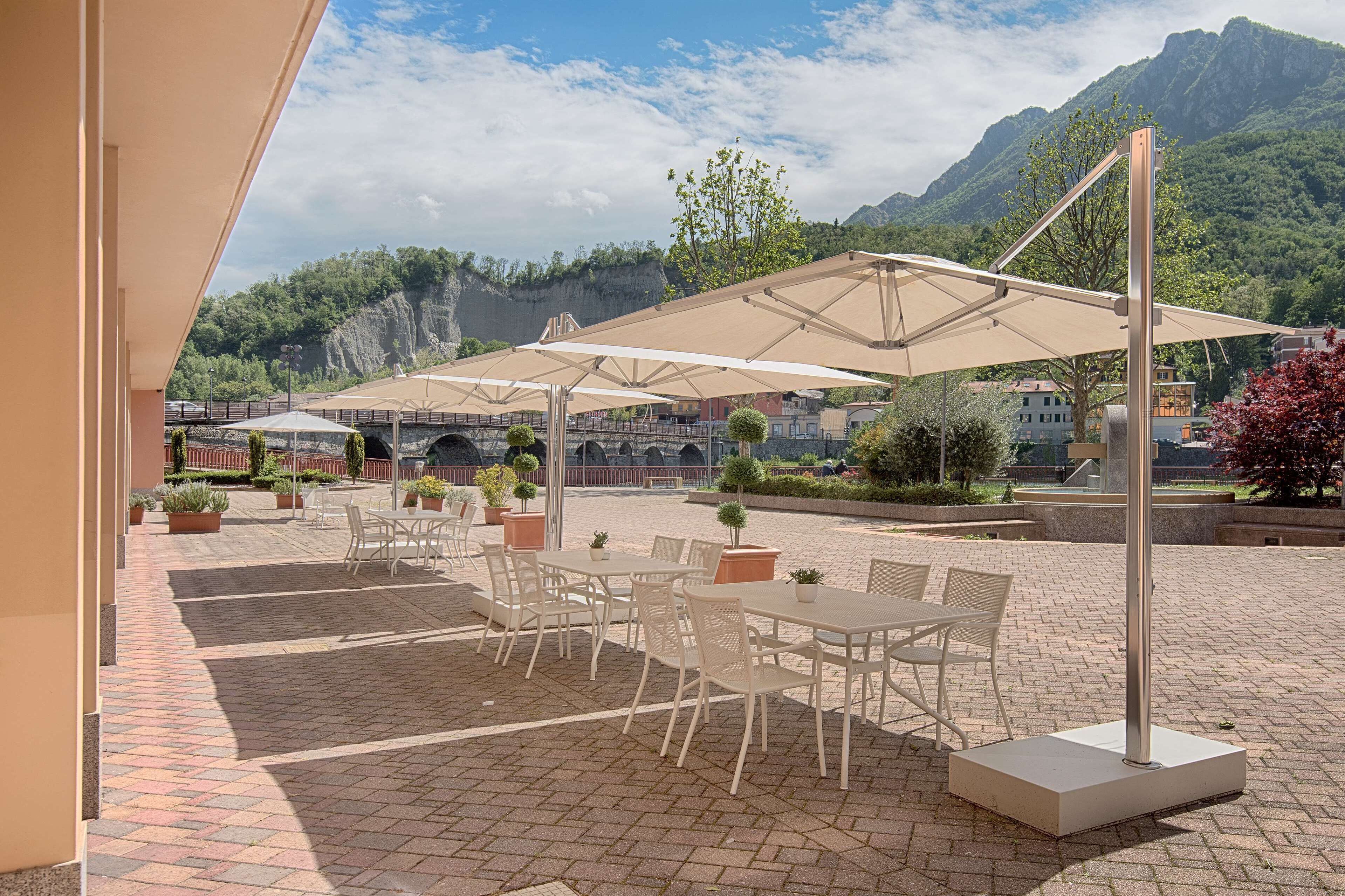 An outdoor seating area with tables and chairs under large umbrellas, overlooking a mountainous landscape.