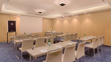 Un salón de conferencias con varias mesas, sillas y una pantalla de proyector.