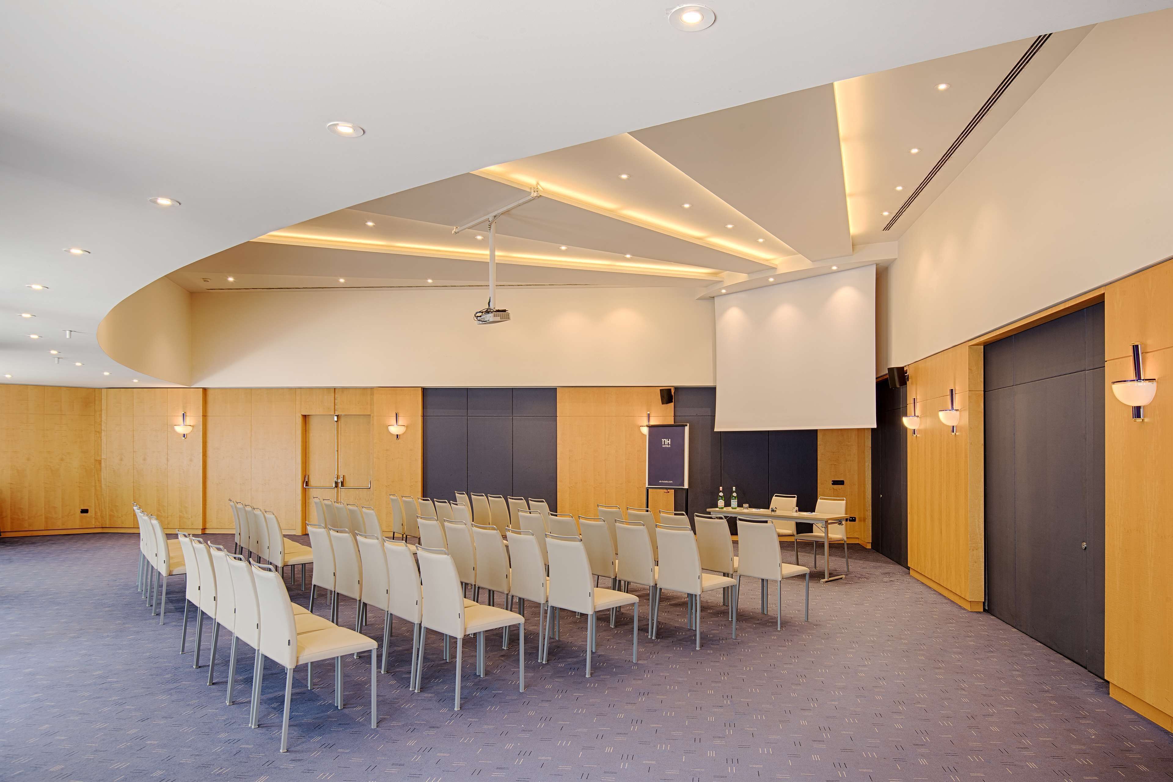 Ett konferensrum med rader av stolar, en projektorduk och en plats för presentationer.