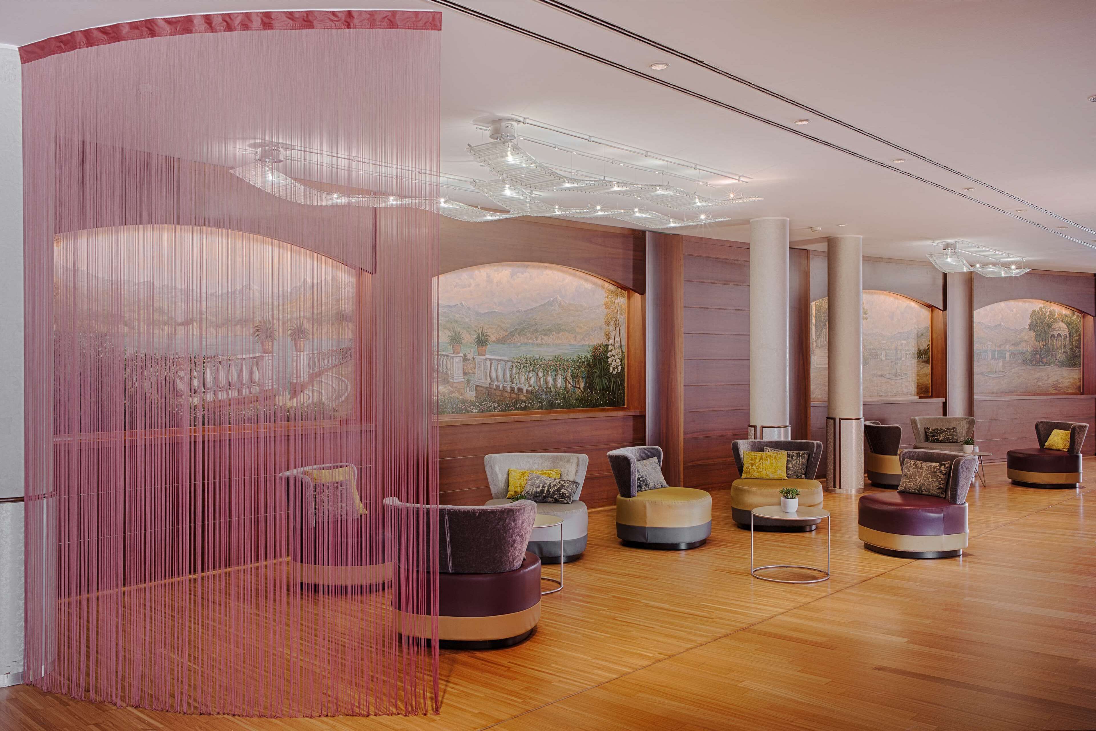 Un hall amplio con asientos modernos, ventanas grandes con vistas a las montañas y una cortina decorativa rosa.