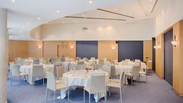 Un salón de conferencias con varias mesas redondas, manteles blancos y sillas.