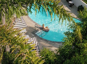 A pool area with a lounge chair, a pool ladder, and surrounding greenery. - The Milo (Santa Barbara)