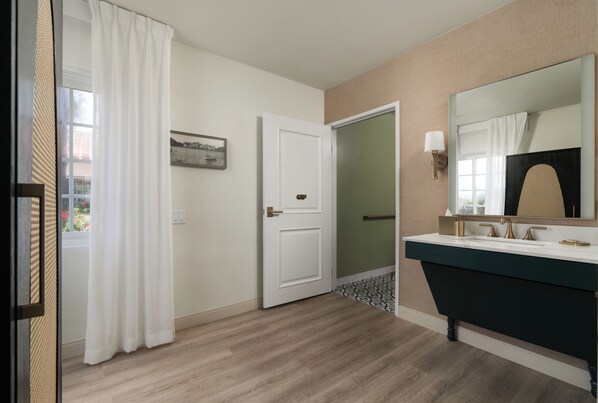 A bathroom with a white door, a mirror, a sink with a dark countertop, and a patterned floor.