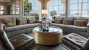 A living room with a round coffee table, two sofas, and a large window with a view of palm trees and a beach.