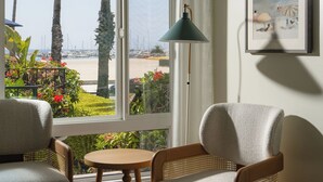 A hotel room with a large window, two chairs, a small table, and a lamp.