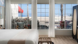 A hotel room with a large window offering a view of the beach and sailboats.