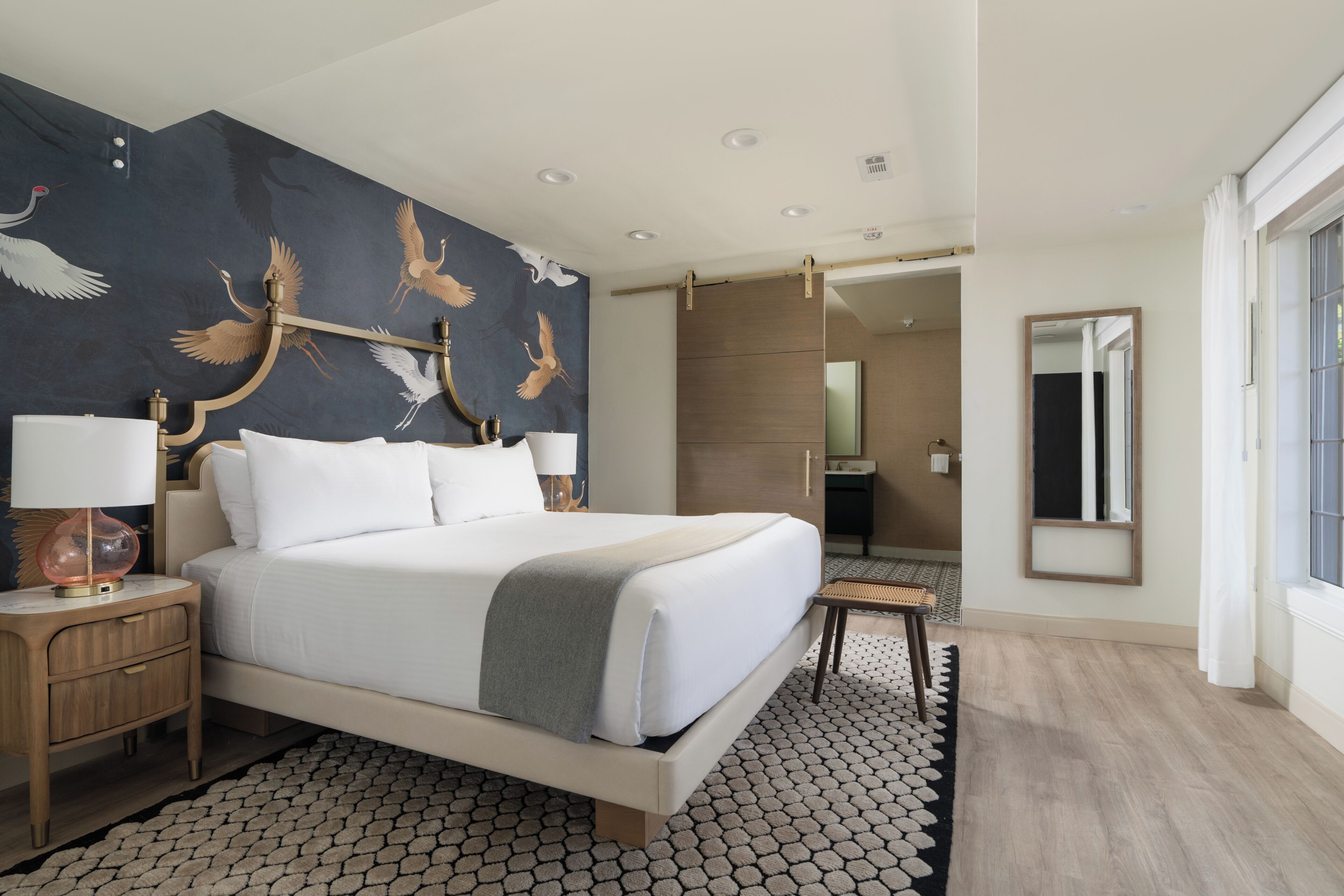 A hotel room with a large bed, a nightstand, a bedside table, a mirror, and a view of the bathroom.