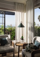 Habitación con vista al mar, con dos sillas, una mesa, una botella y vasos, además de una lámpara.