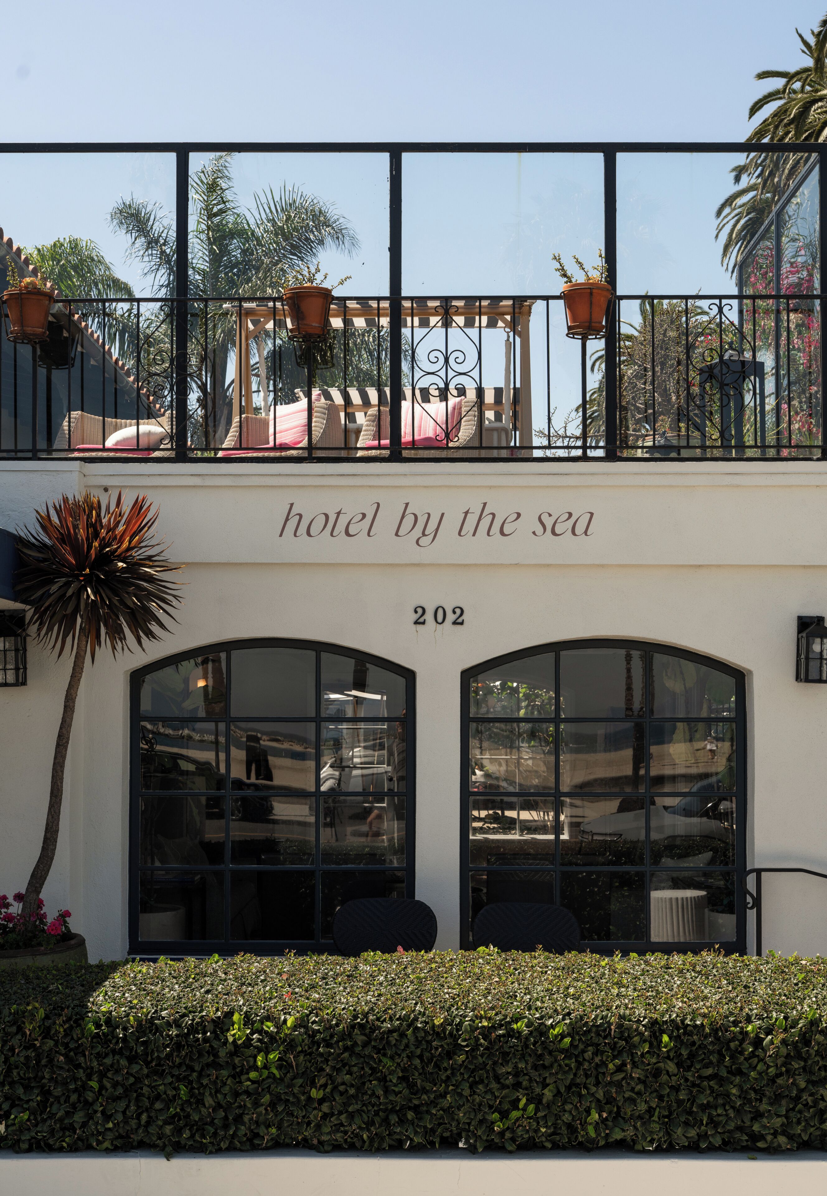 A hotel with a balcony, potted plants, and a sign reading 'hotel by the sea'.