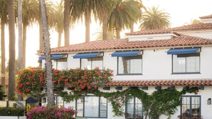 A two-story building with a tiled roof, multiple windows, and a well-maintained garden with flowering plants and a tree.