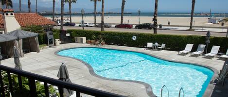 A swimming pool with lounge chairs and umbrellas, a beach view, and palm trees.
