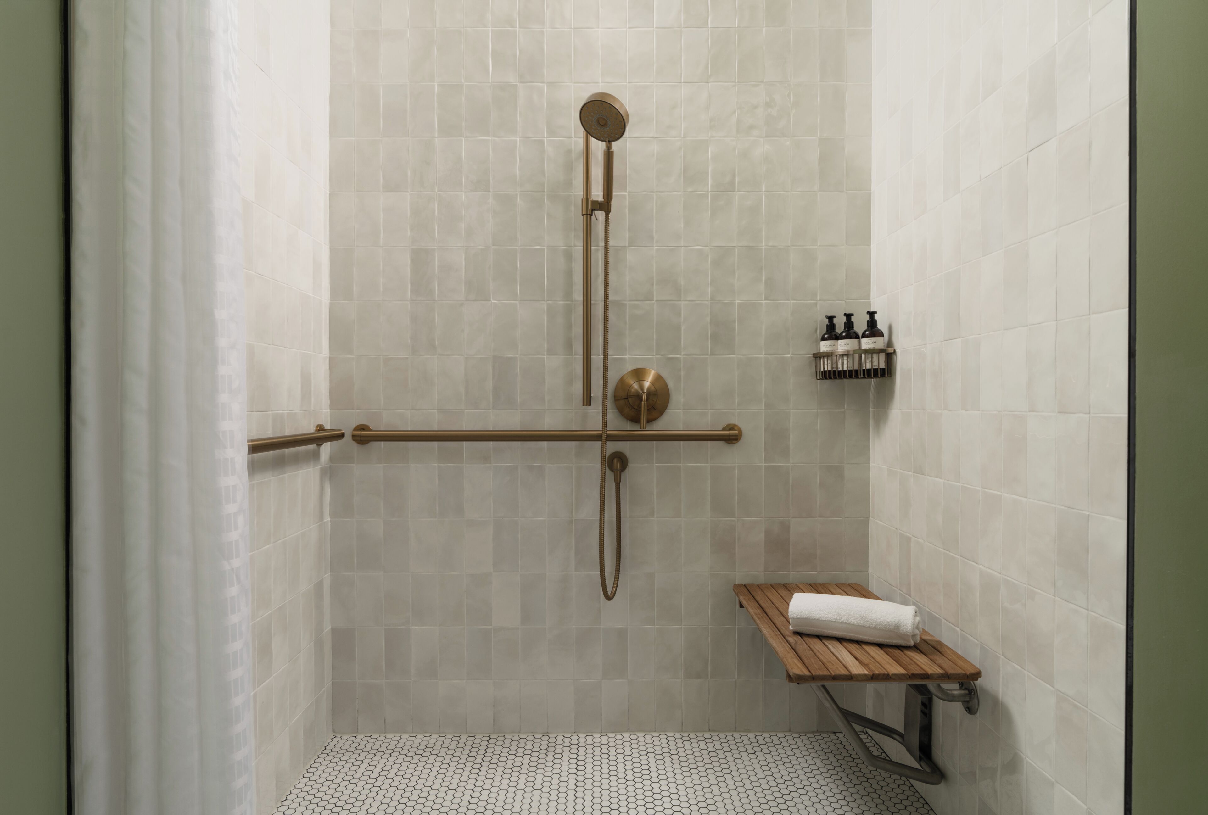 A shower area with a handrail, a showerhead, and a shelf with toiletries.