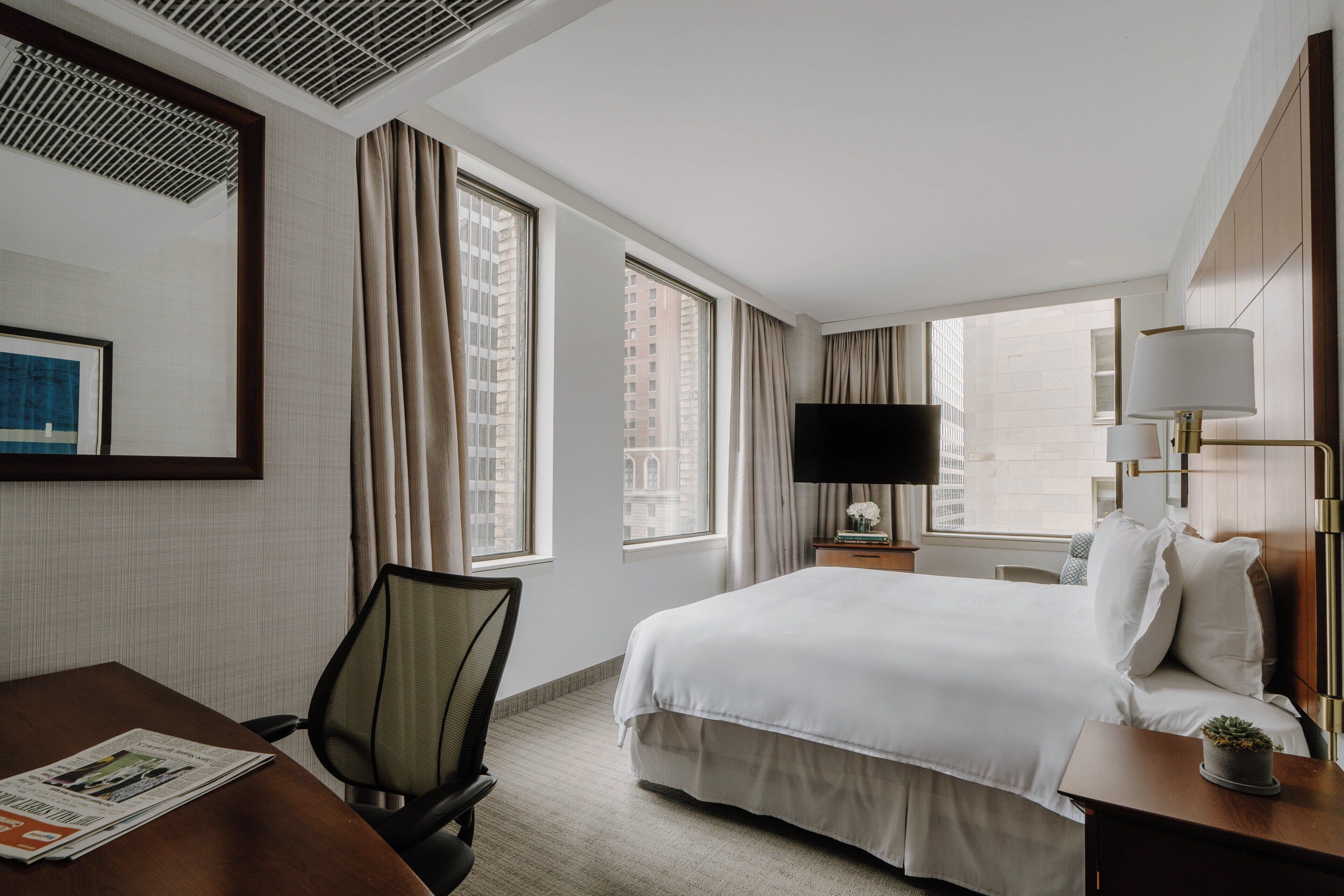 Une chambre d’hôtel avec un grand lit, un bureau, une chaise, une télévision et une fenêtre avec des rideaux.