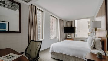 Una habitación de hotel con una cama grande, un escritorio, una silla, un televisor y una ventana con cortinas.