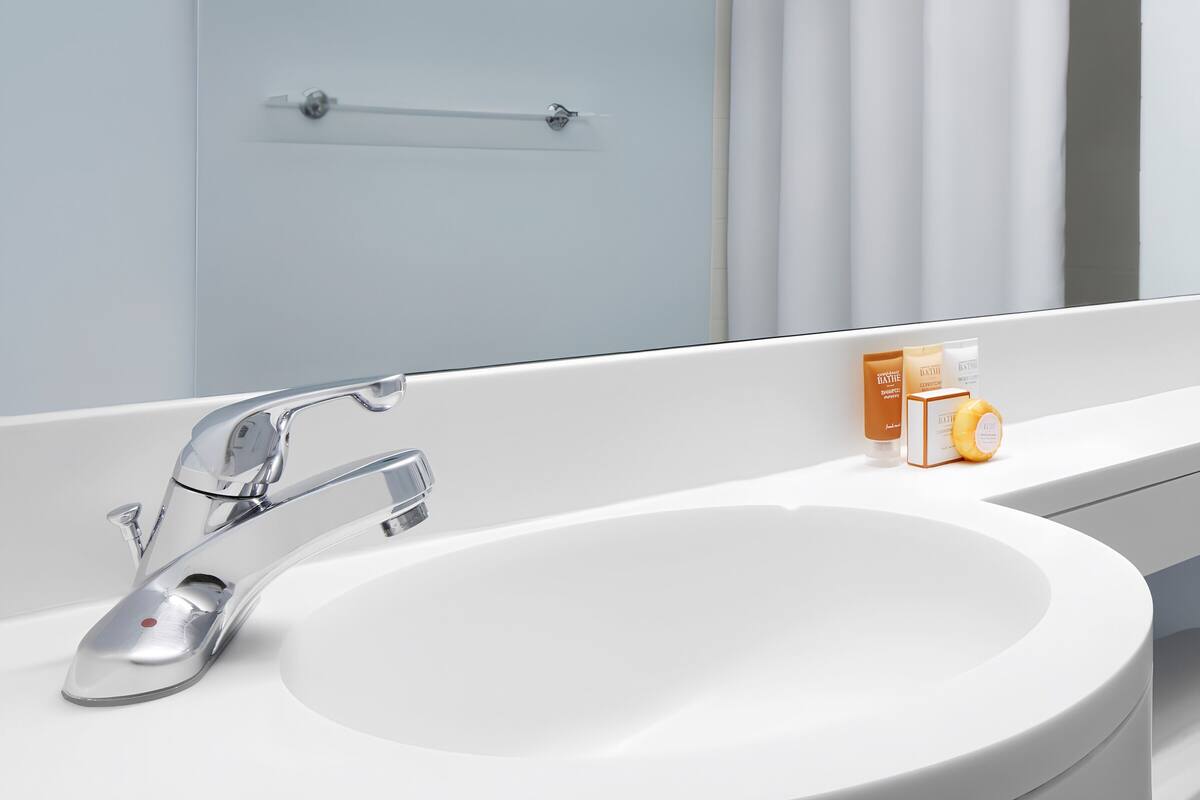 A bathroom with a white sink, chrome faucet, and a mirror reflecting a door and curtains.