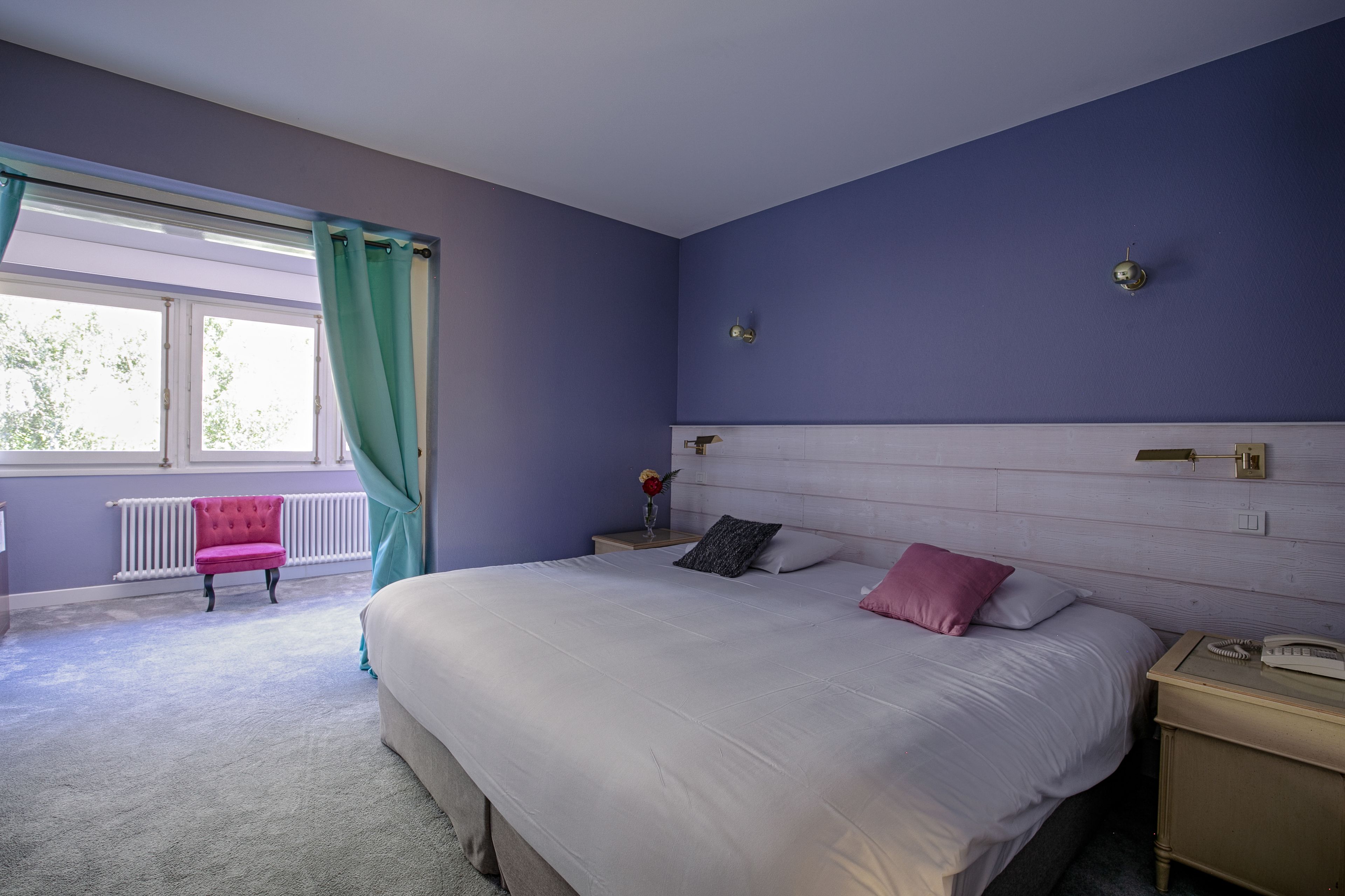Un dormitorio con una cama grande, una mesita de noche, una silla y una ventana con cortinas.