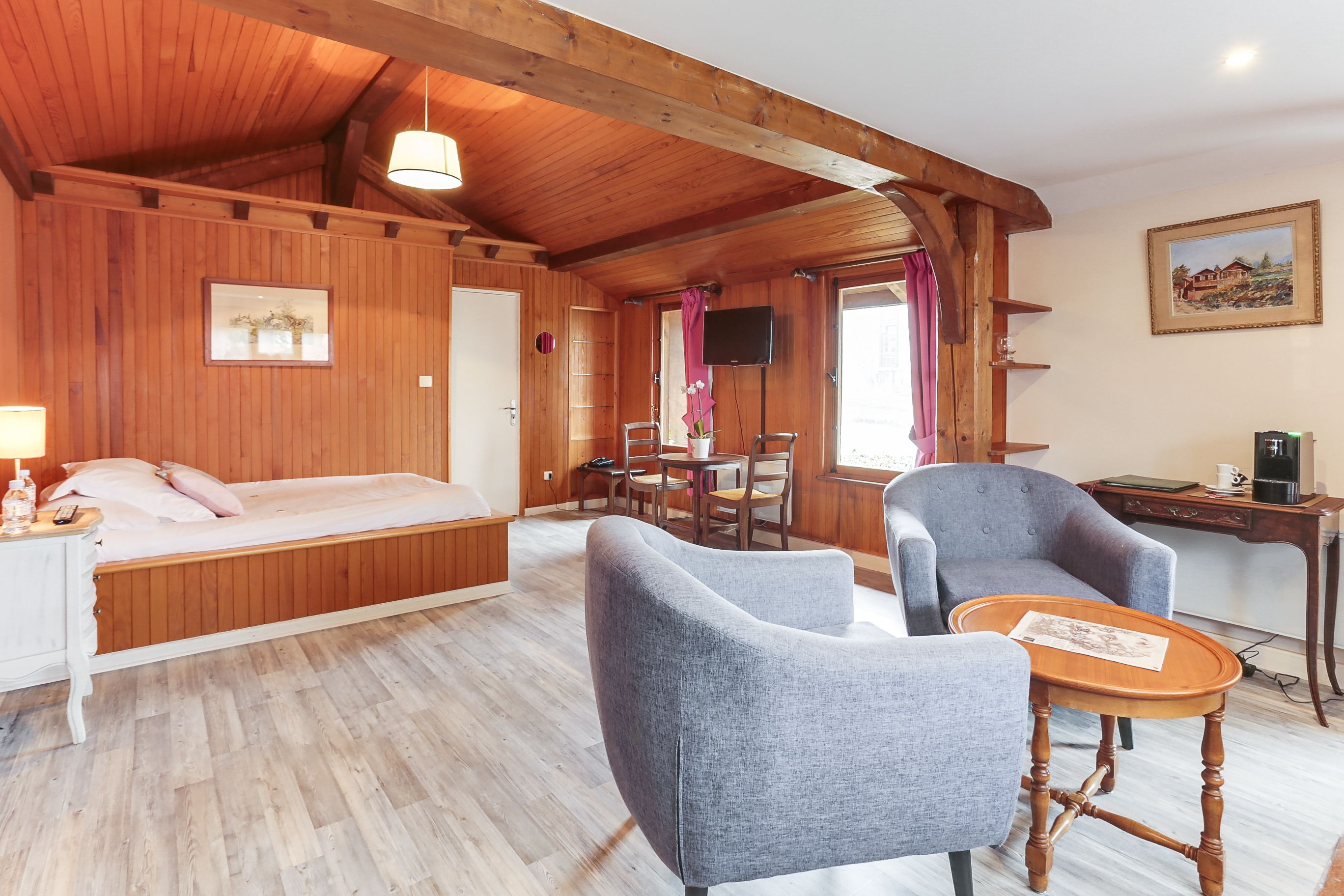Un intérieur en bois comprenant un lit, deux fauteuils, une petite table, un téléviseur et un tableau accroché au mur.