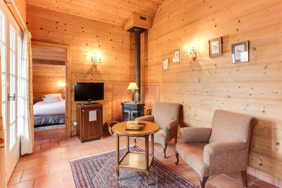 A cozy log cabin room with a bed, a television, a table, and two armchairs.