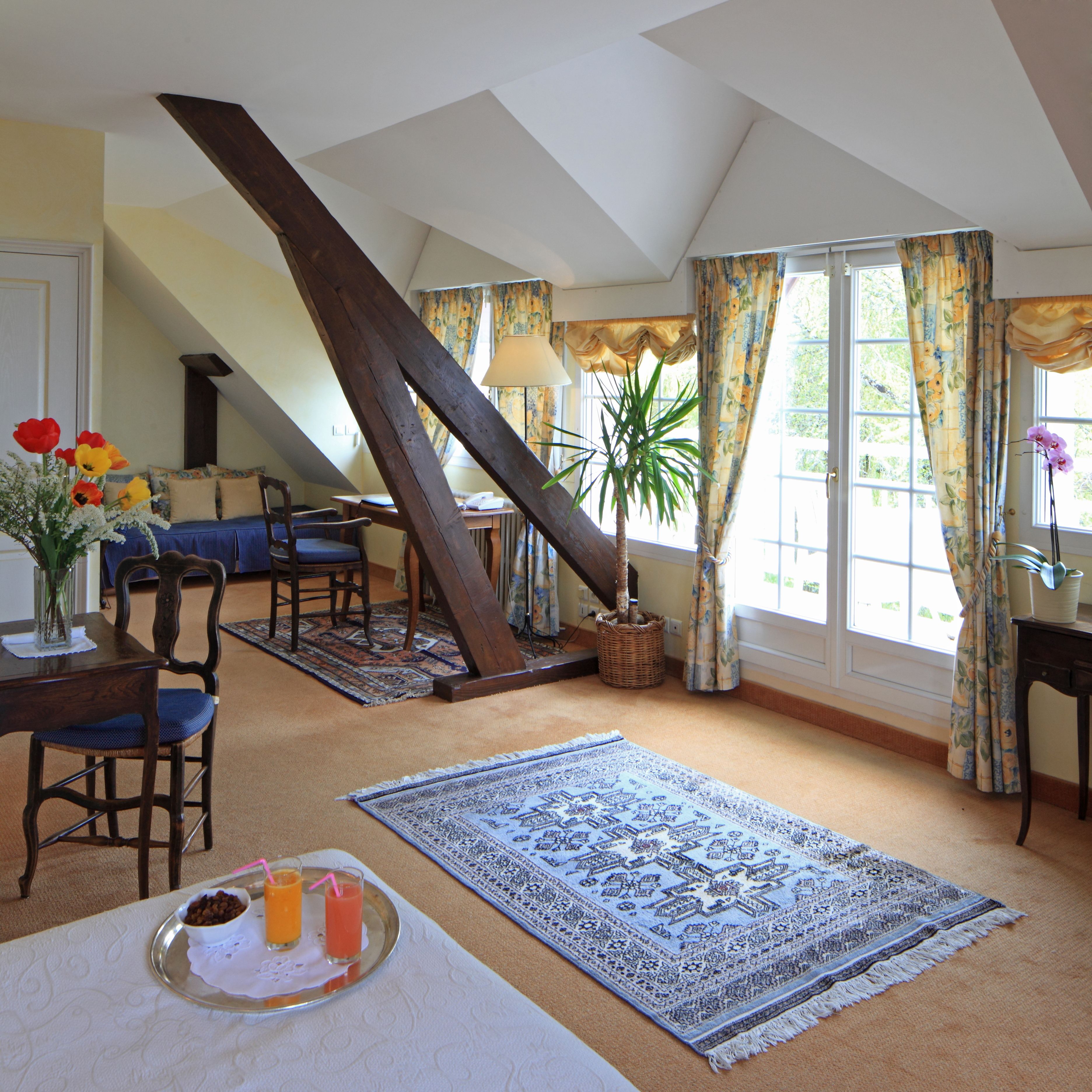 A cozy room with a sloped ceiling, a dining area with a table and chairs, a large window with curtains, and a potted plant.