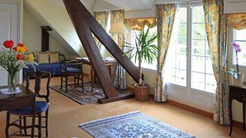 A cozy room with a sloped ceiling, a dining area with a table and chairs, a large window with curtains, and a potted plant.