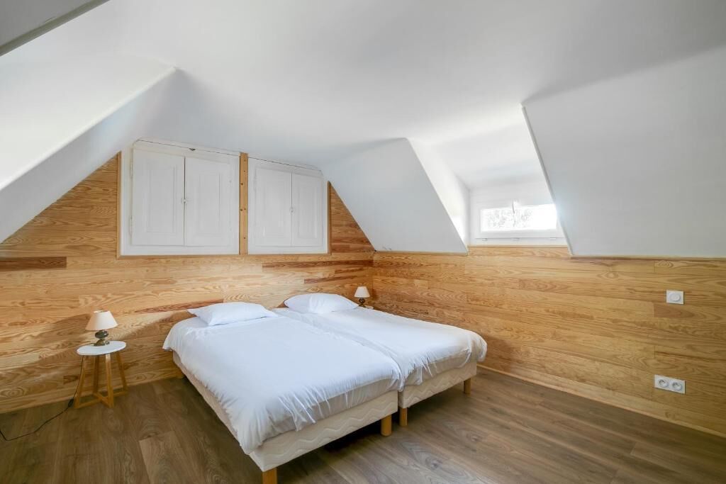 Een slaapkamer met een schuine kap, houten wanden, twee bedden, bedlampen en een raam.