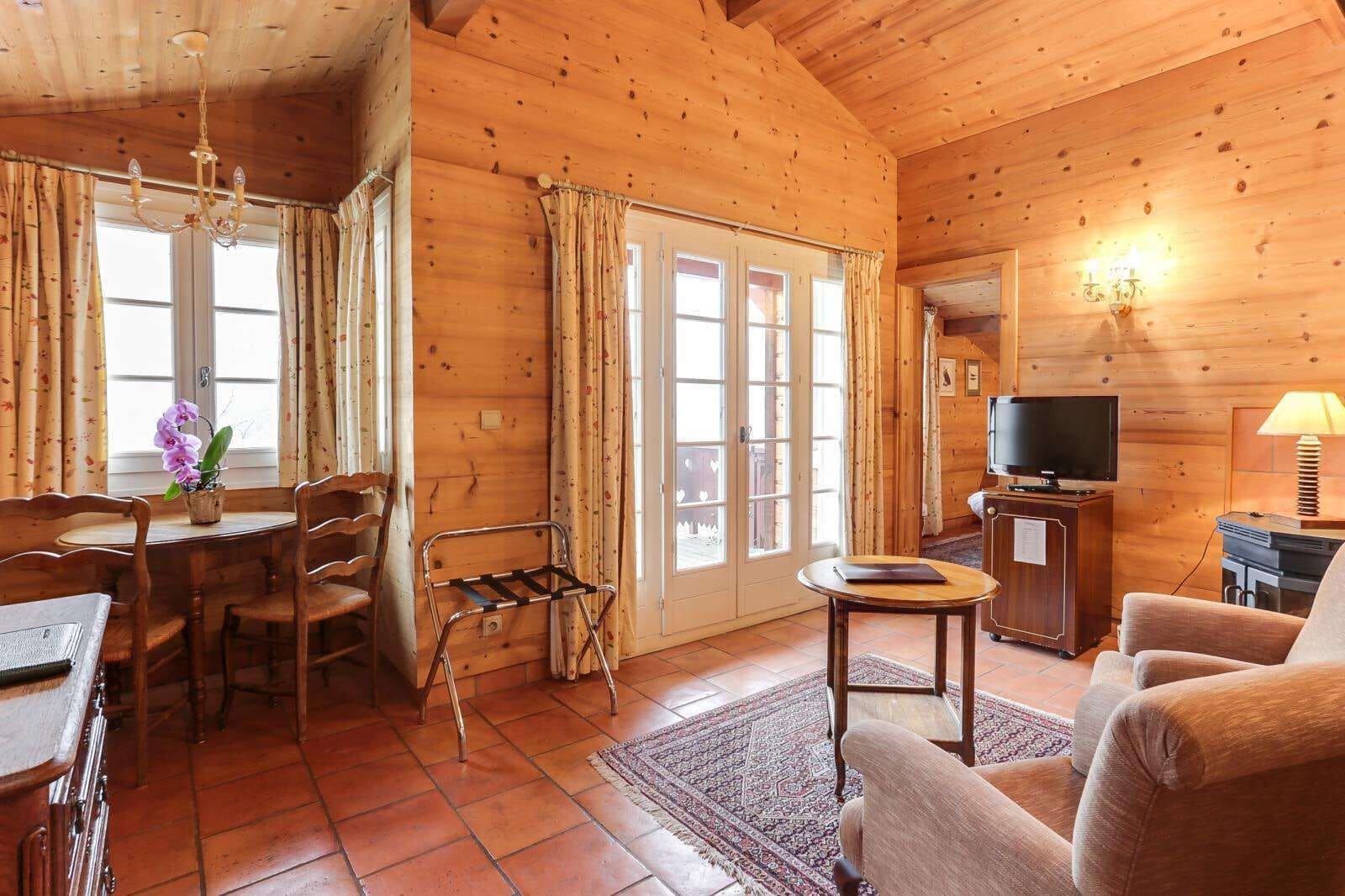 A wooden cabin interior with a dining area, a sofa, a TV, and a lamp.