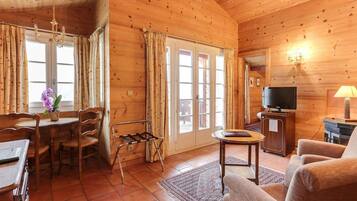 A wooden cabin interior with a dining area, a sofa, a TV, and a lamp.