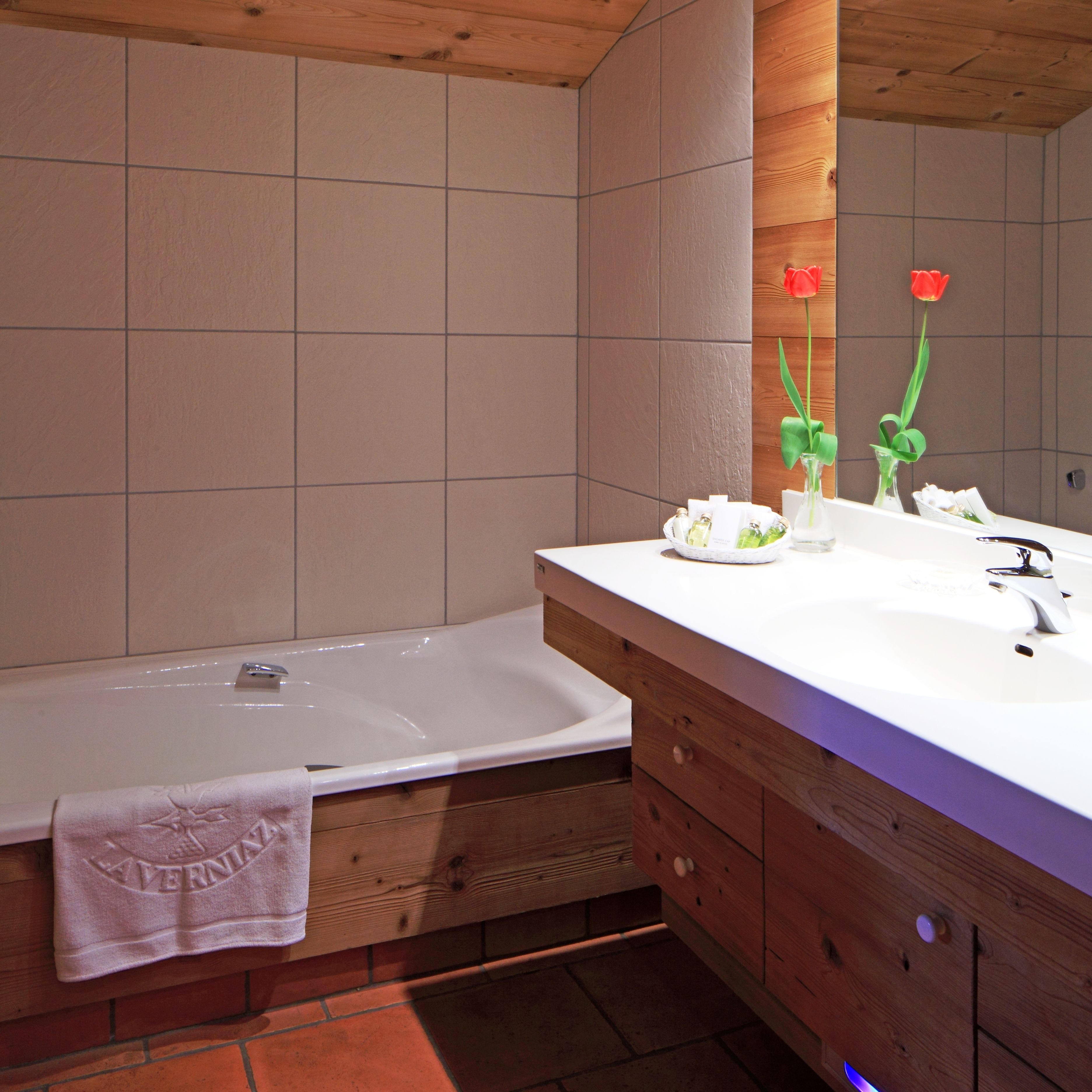 Un baño moderno con tocador de madera, una bañera blanca y un espejo que refleja una tulipán roja.