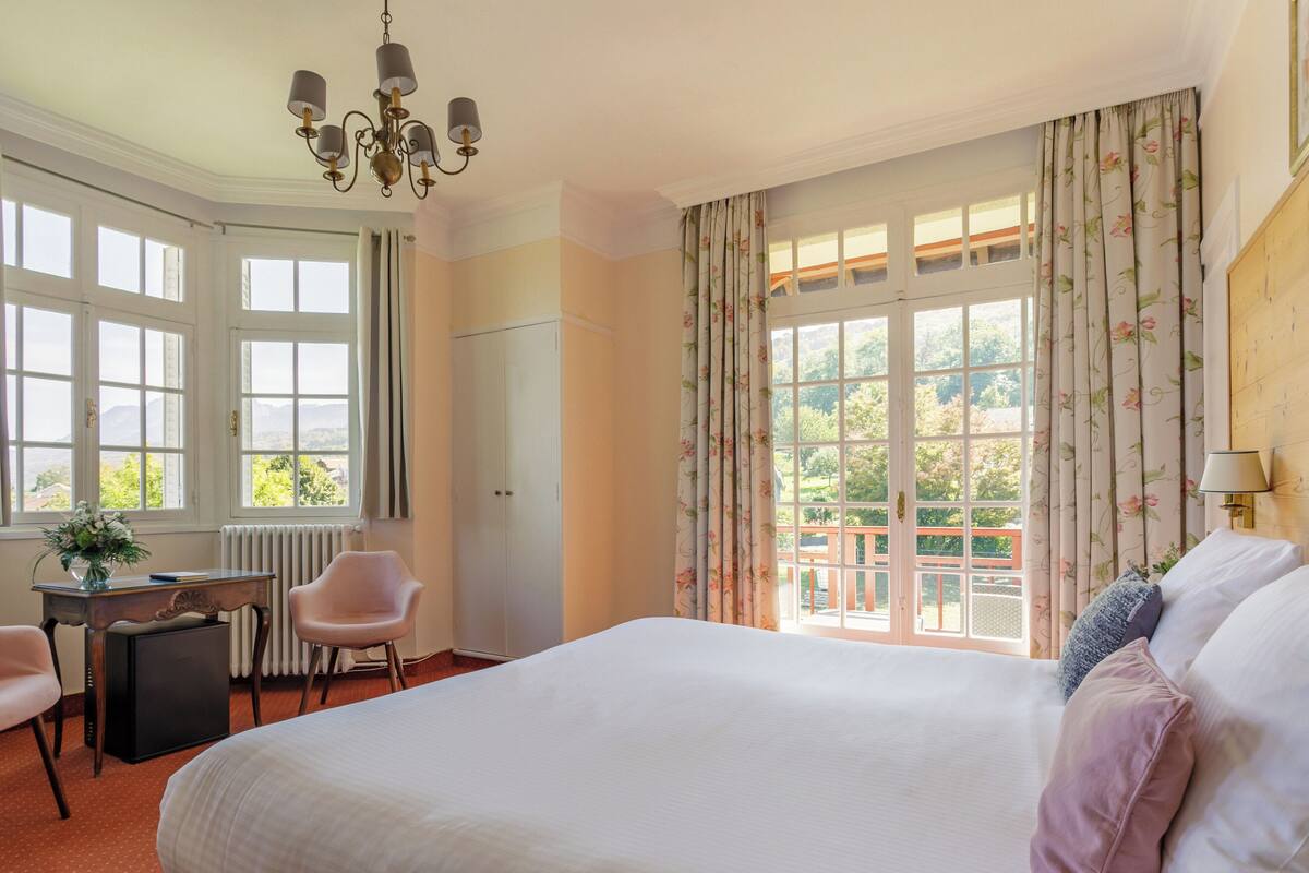 A bedroom with a large bed, a desk, a chair, and a radiator.