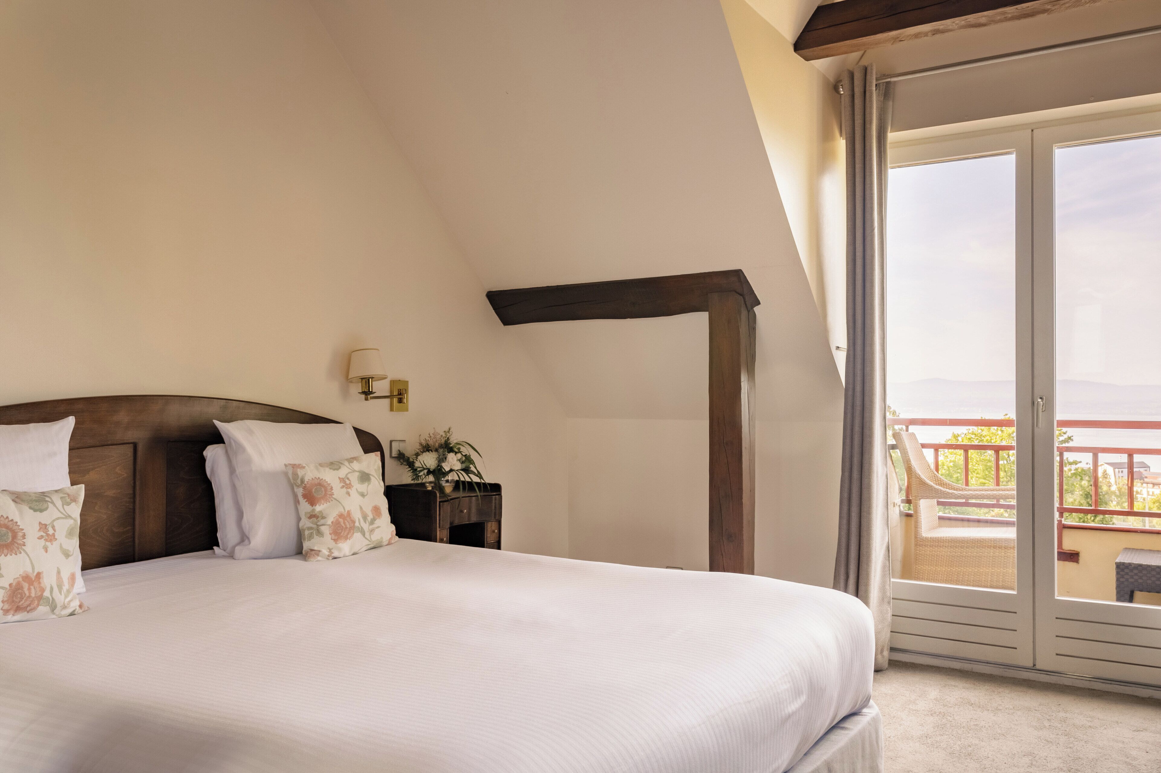 A bedroom with a large bed, a nightstand, a lamp, and a view of the outside balcony.